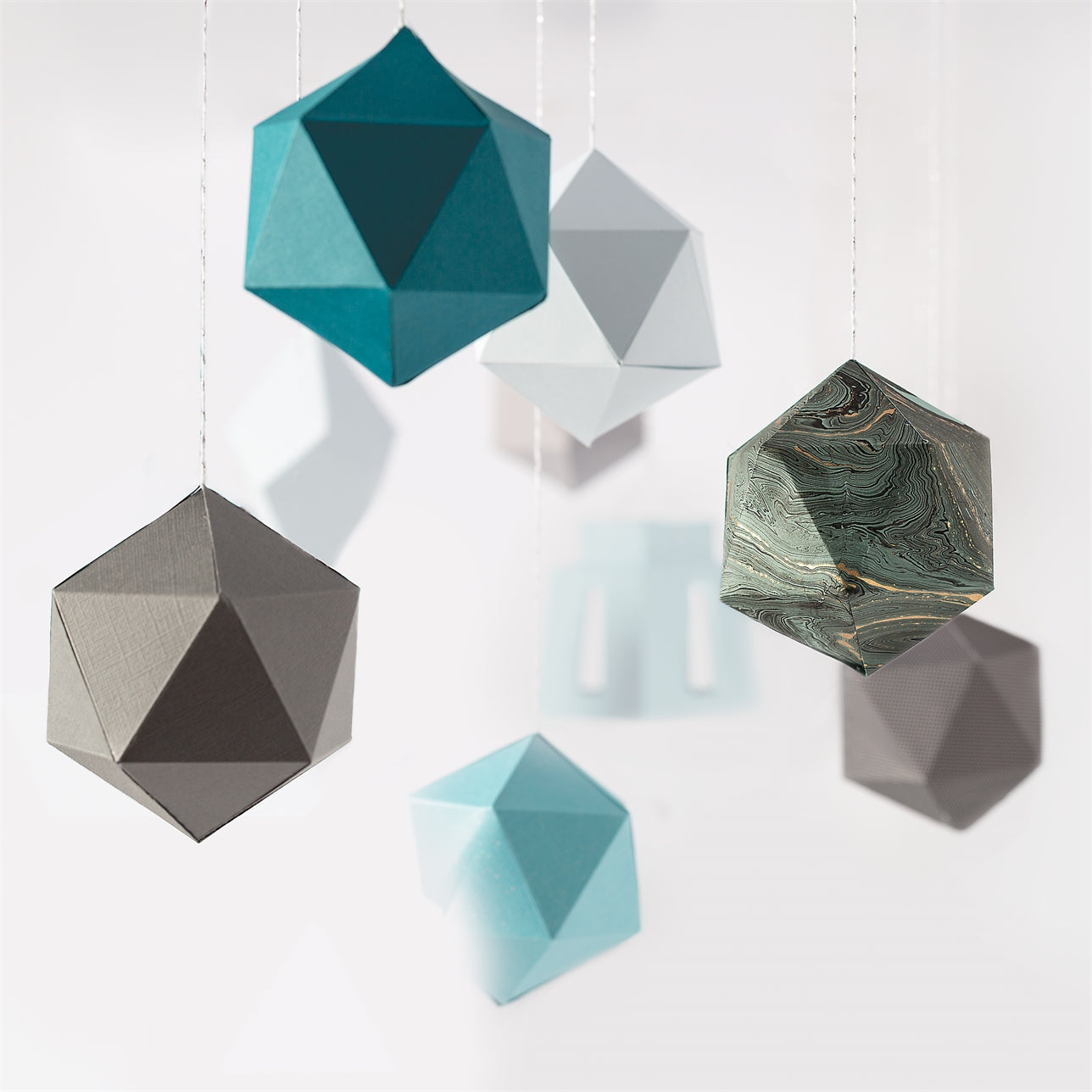 Several 3D paper geode templates in various colors and patterns hang against a white background.
