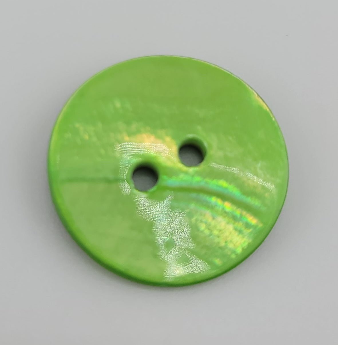 A round, lime green shell button with two holes and iridescent highlights.