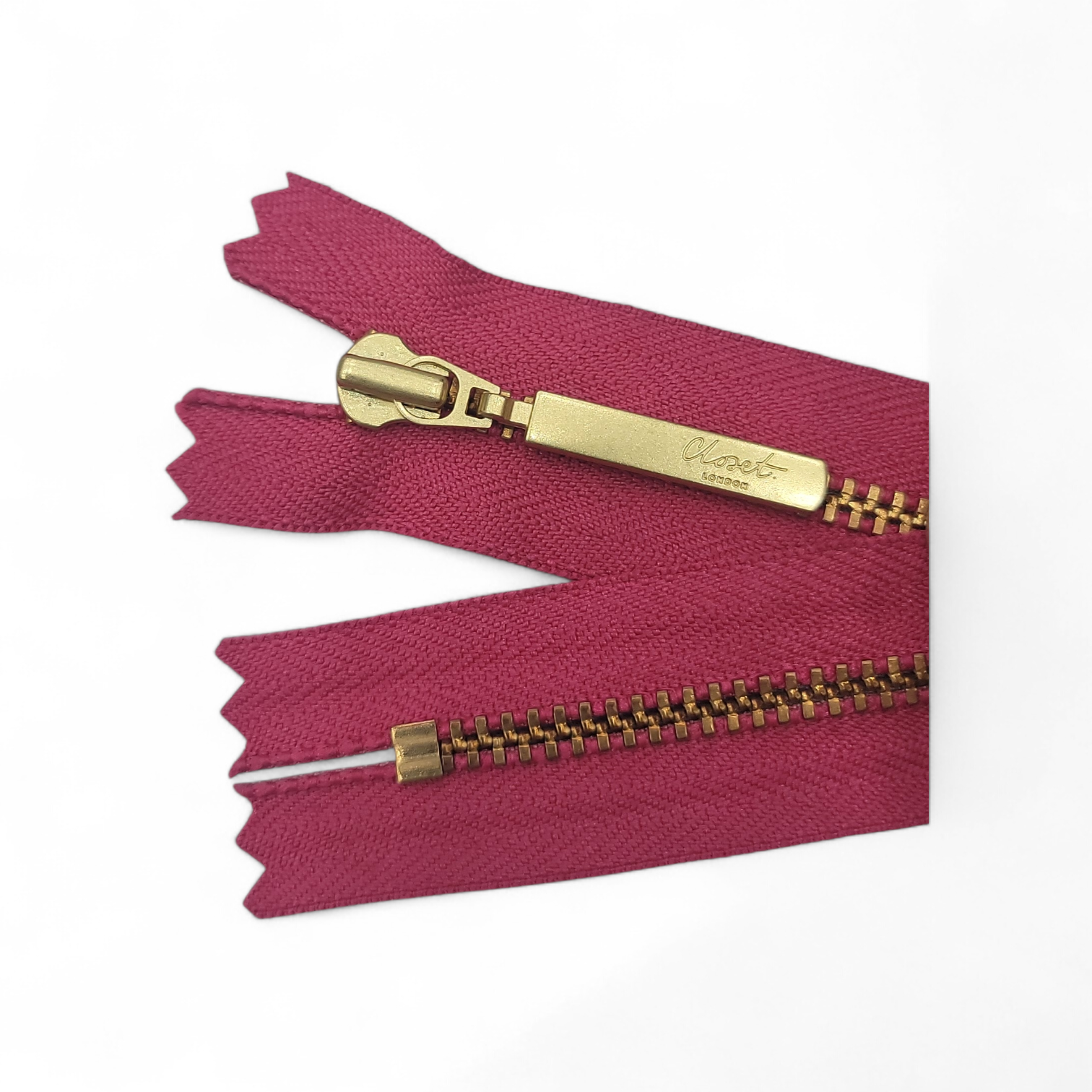 YKK size 3 closed end gold metal zipper on a pink fabric.