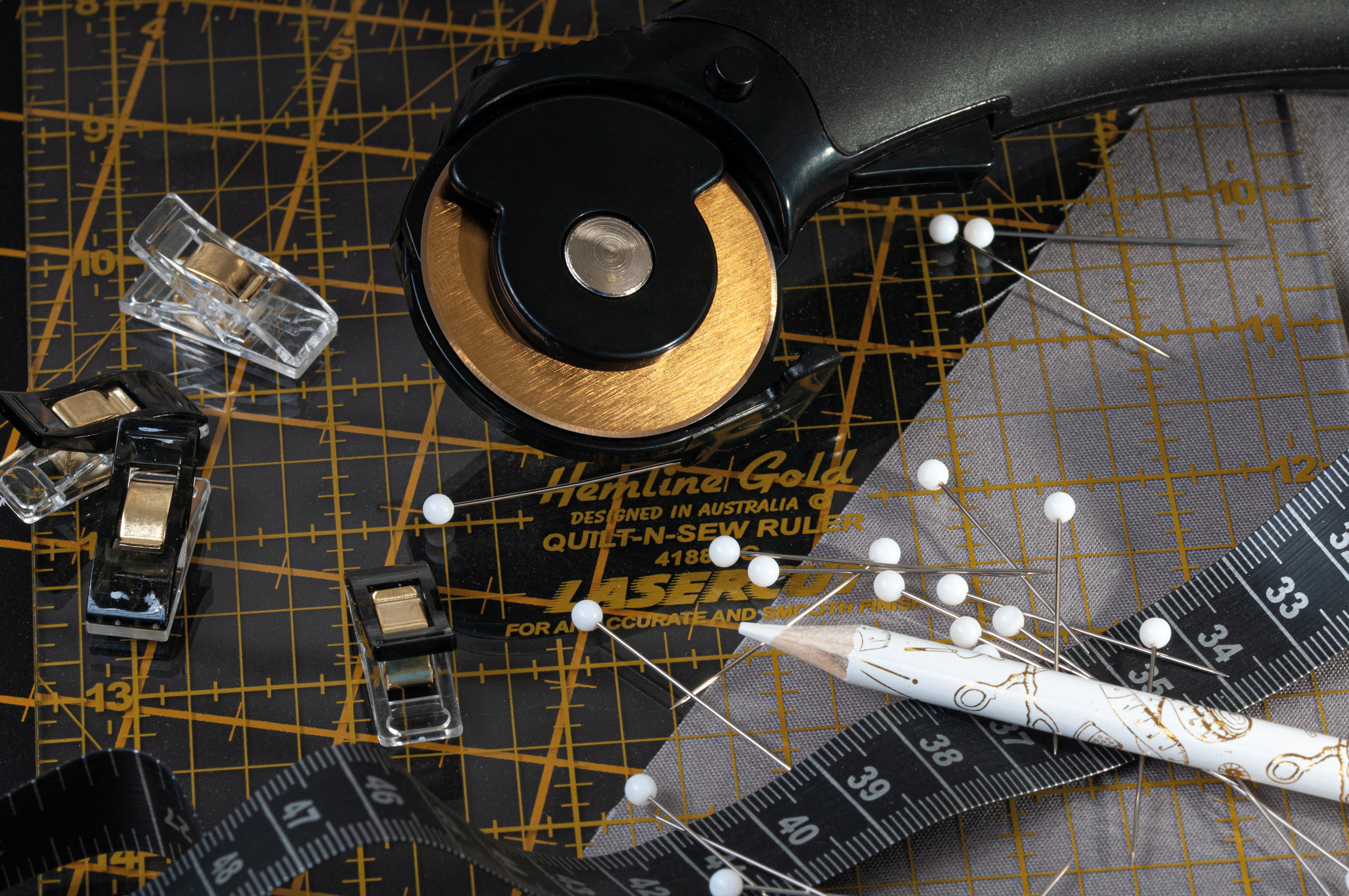 Hemline self-healing cutting mat with gold imperial markings, rotary cutter, and sewing tools.