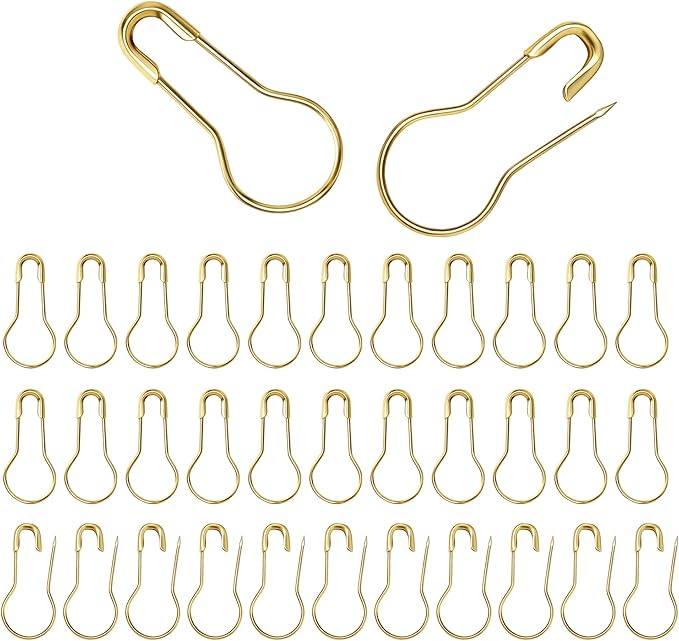 A collection of gold-colored metal bulb safety pins arranged in rows on a white background.