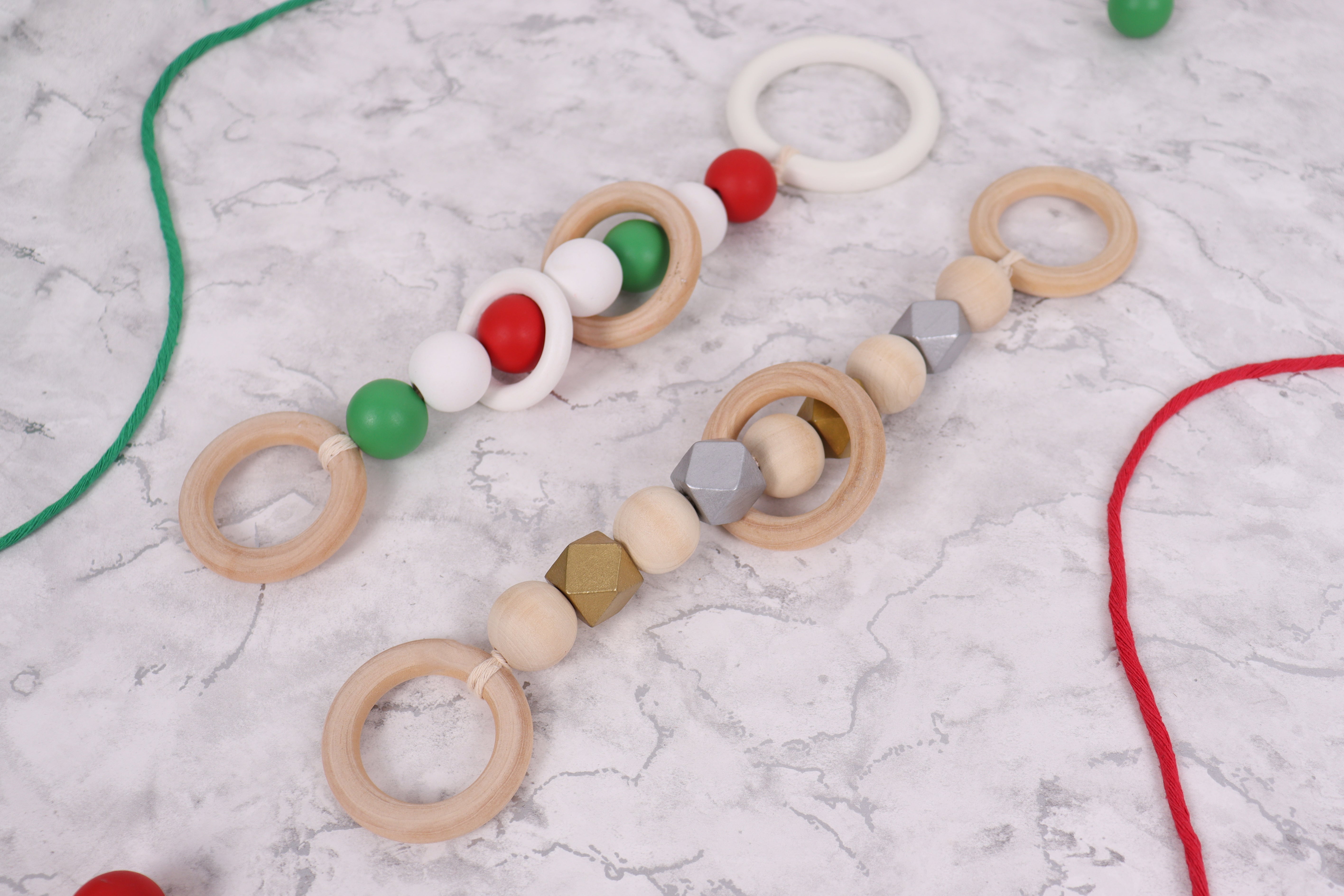Two handmade Christmas macramé bead ornaments with wooden rings on a marble surface.