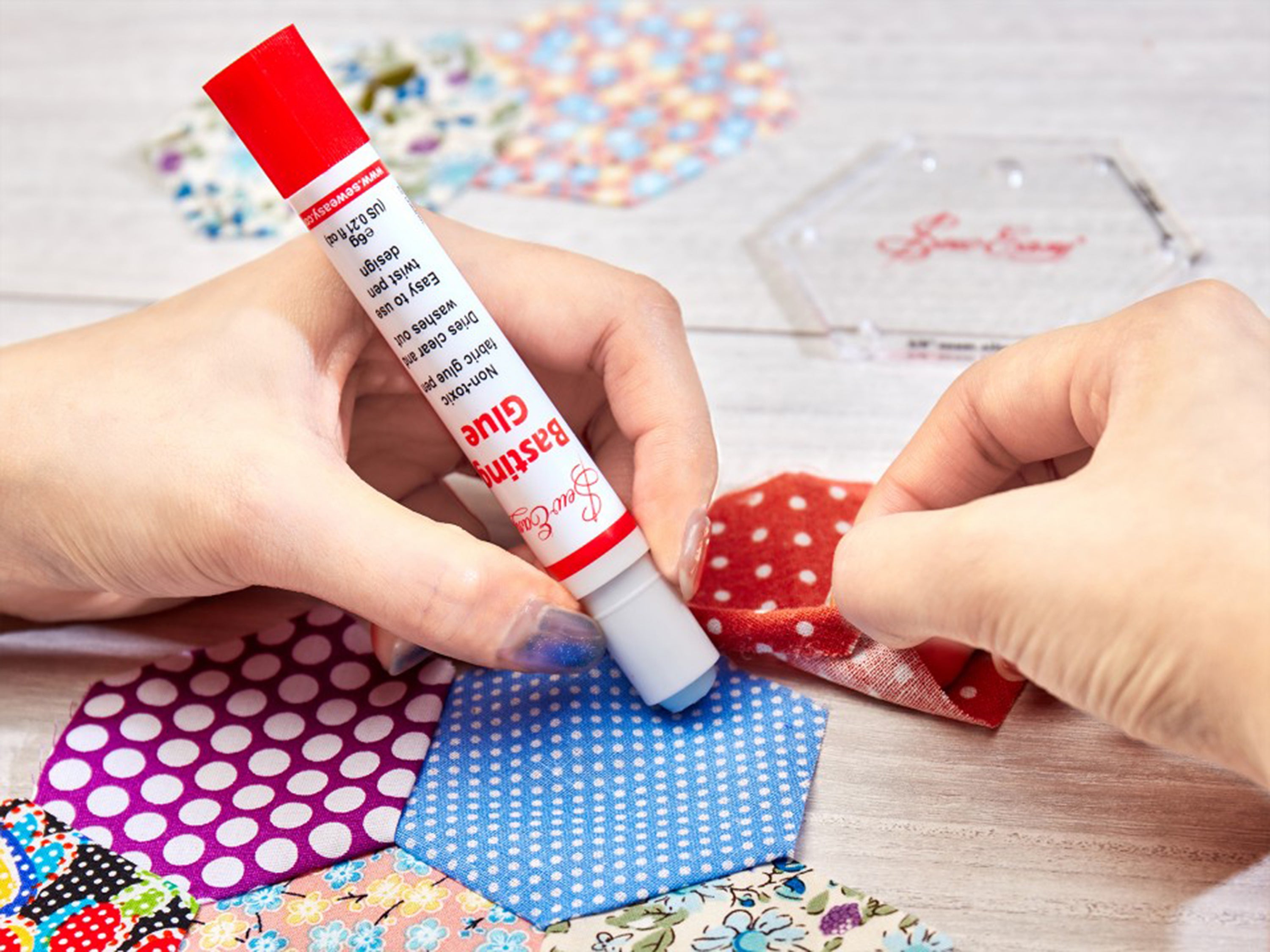 A person uses a Seweasy Basting Glue pen to apply temporary adhesive to hexagonal fabric pieces.