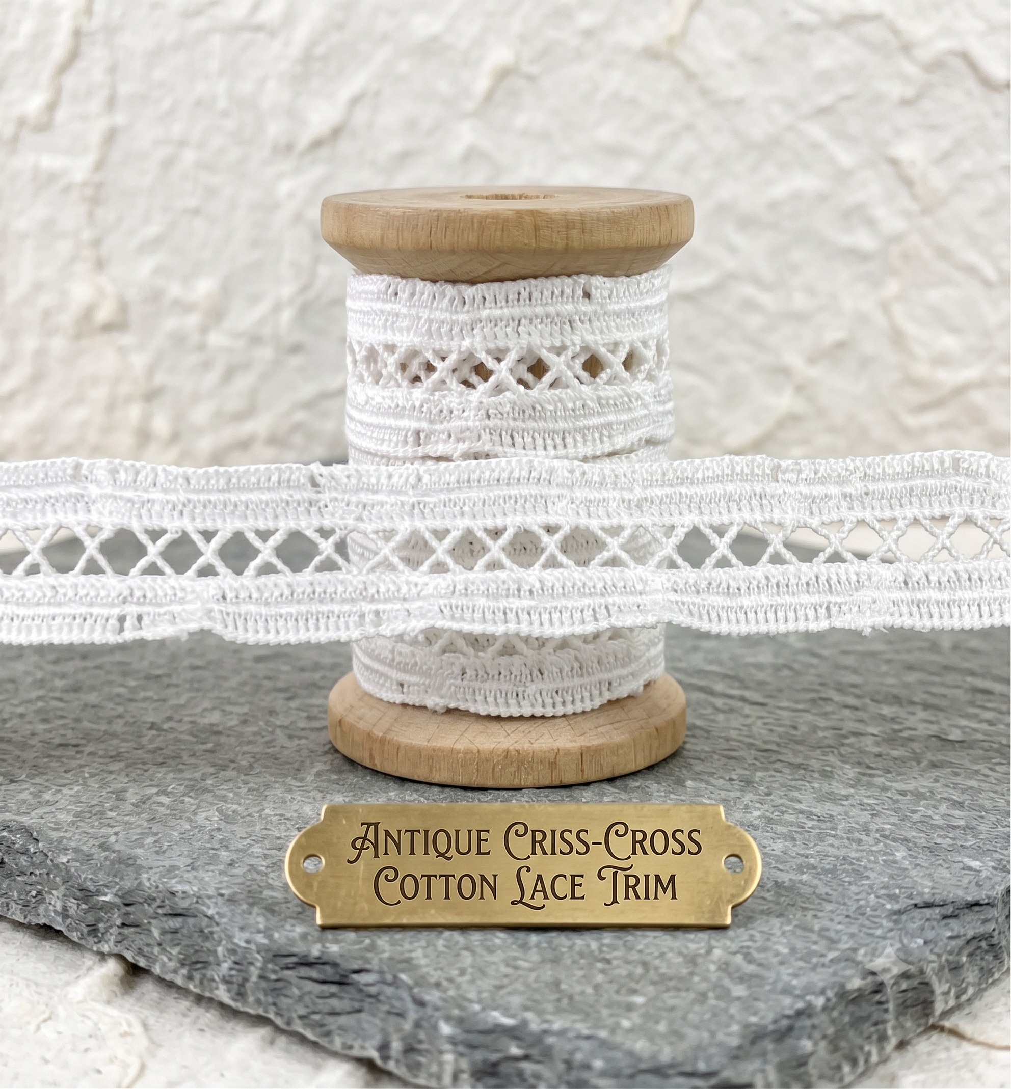 White criss-cross cotton lace trim wrapped around a wooden spool on a slate surface.