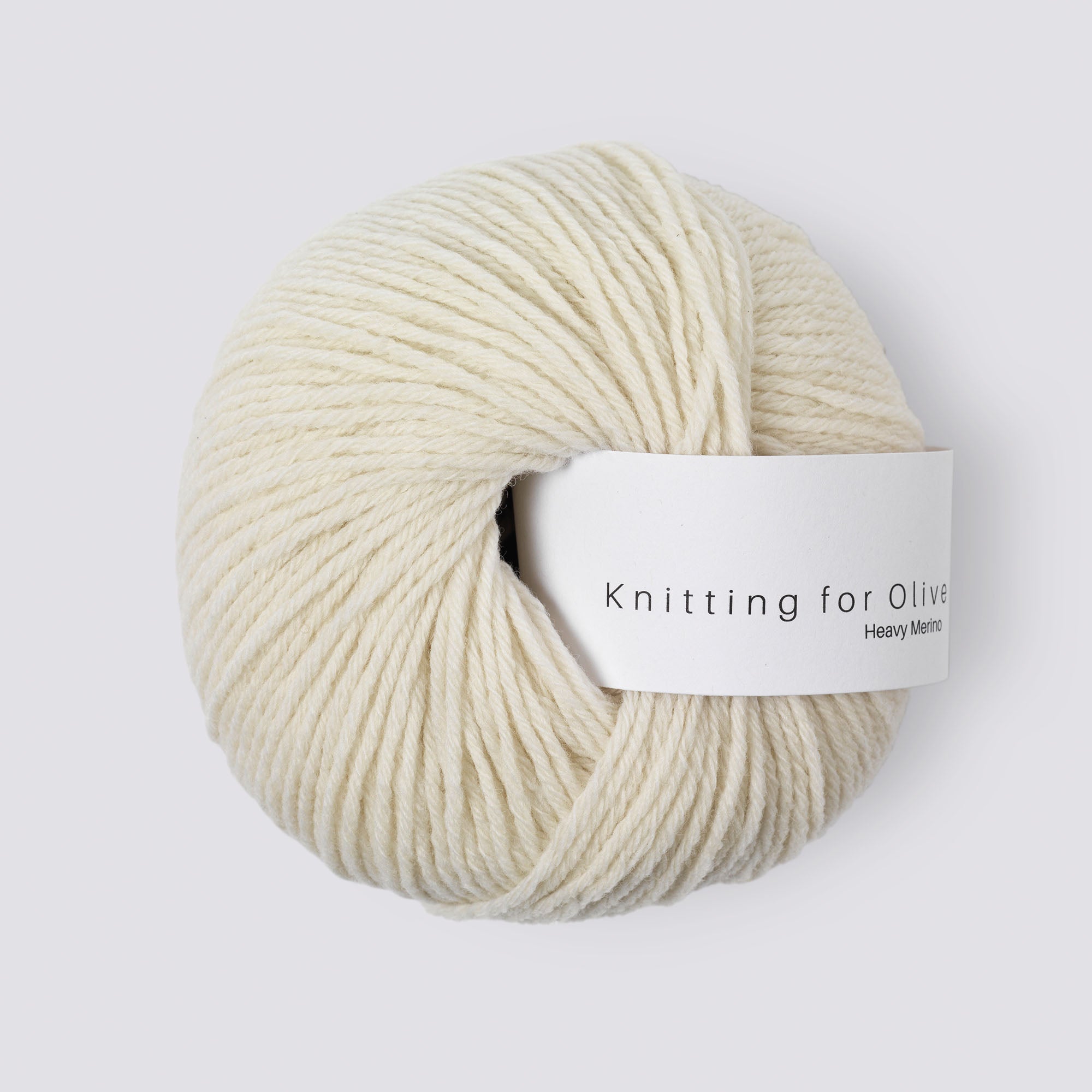A ball of cream-colored Heavy Merino wool yarn with a white label that reads "Knitting for Olive Heavy Merino".