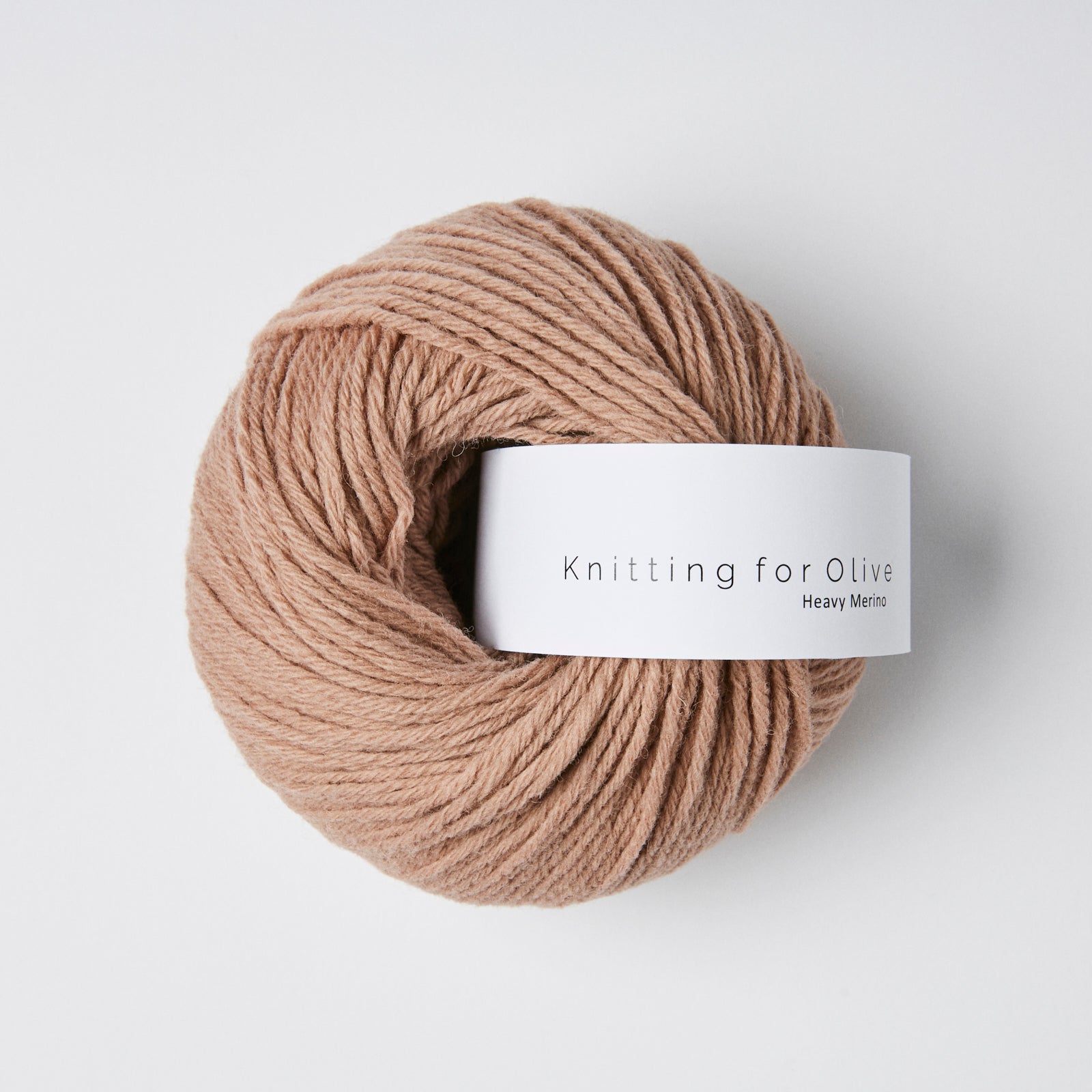 A ball of tan Heavy Merino wool yarn with a white label that says "Knitting for Olive Heavy Merino".