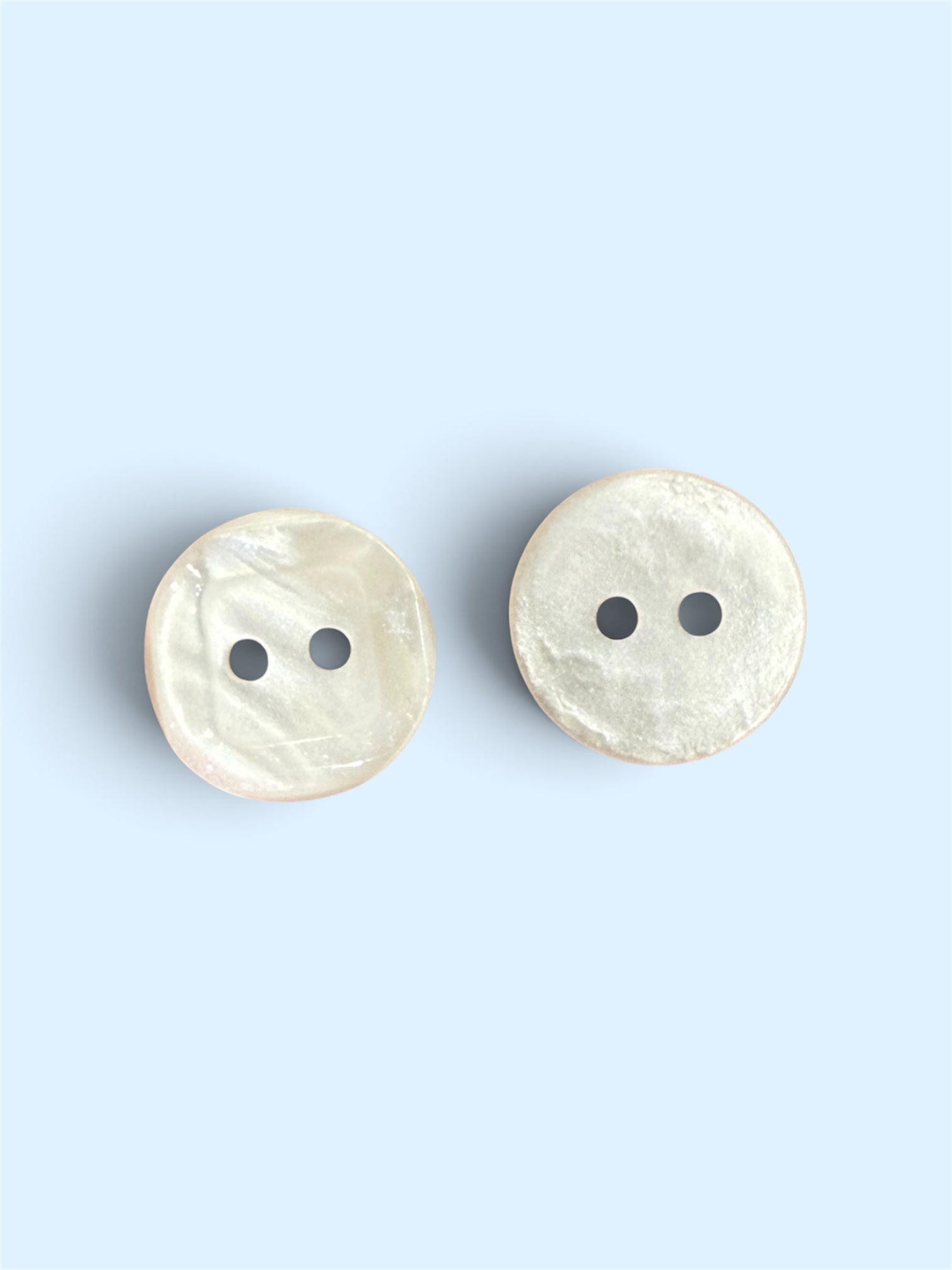 Two 12mm white resin round square buttons with a glossy finish and two holes on a light blue background.