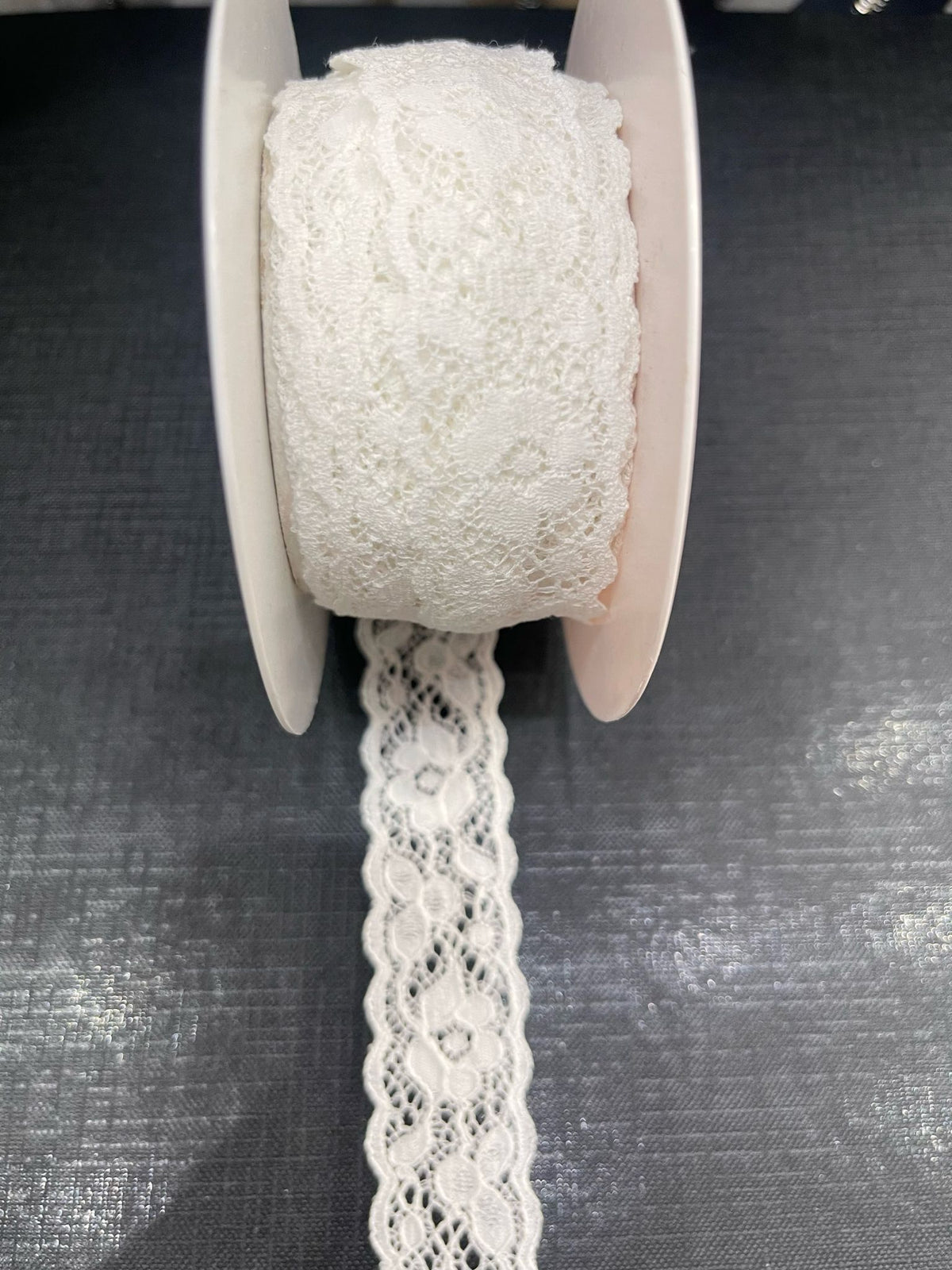White crochet lace ribbon on a spool, with a length of ribbon unspooled.