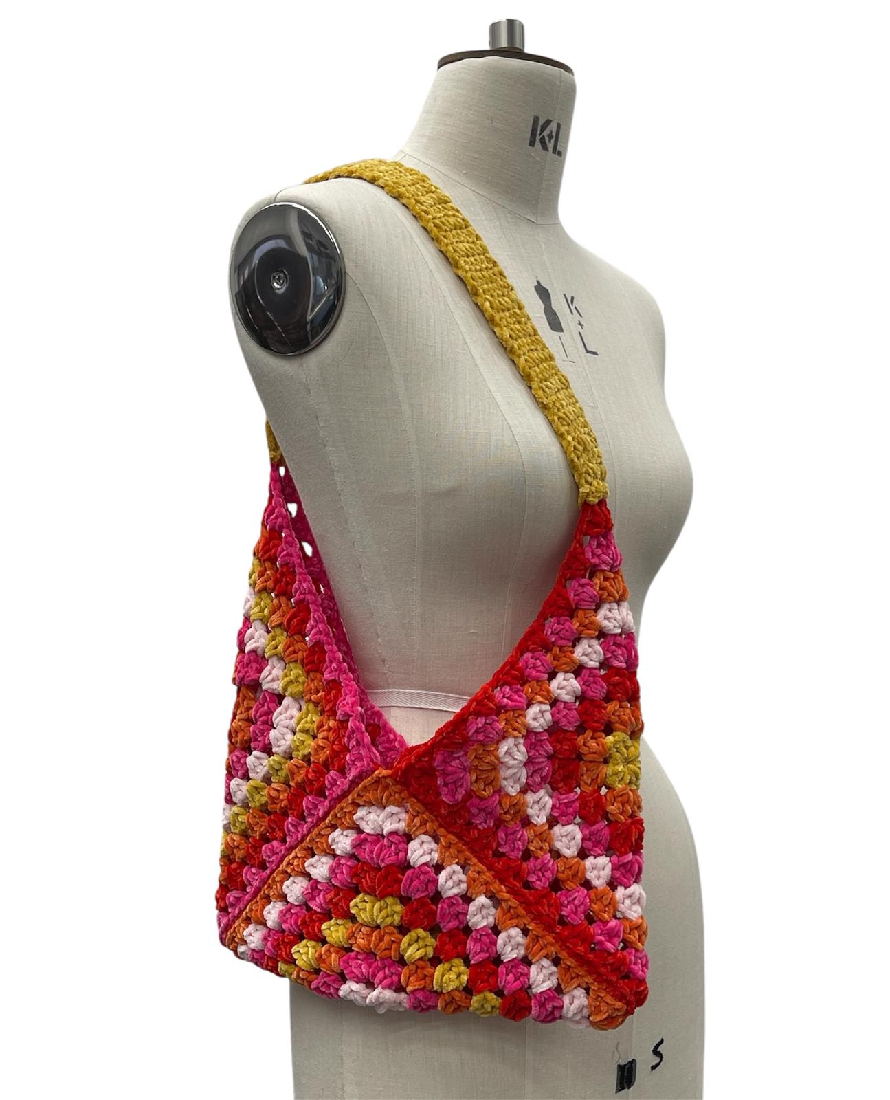 Handmade crochet bag in mixed colors with a yellow strap on a mannequin.