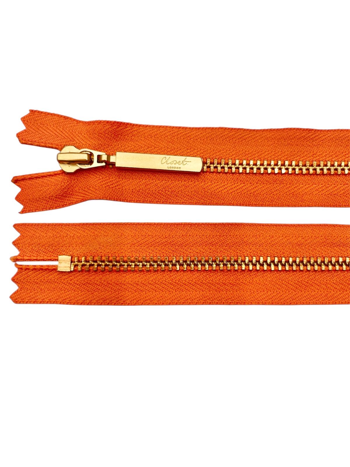 Orange YKK closed end zipper with gold metal teeth and pull tab.