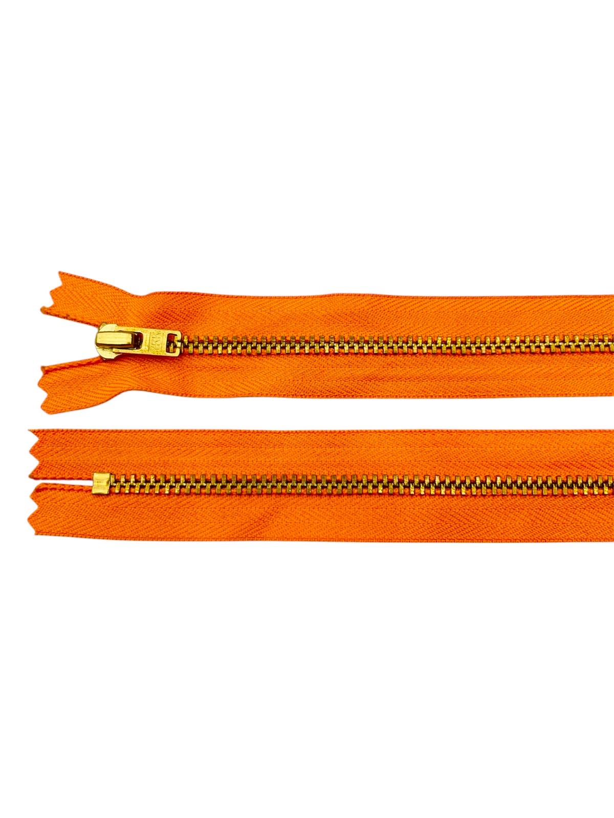 YKK Size 3 closed end gold metal zipper on orange fabric.