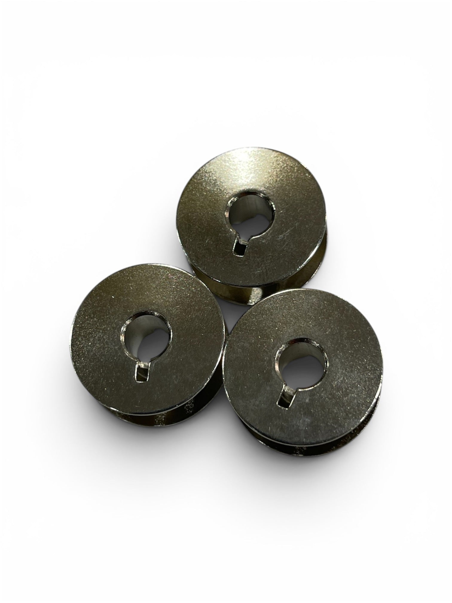 Three silver Janome Class 15 metal bobbins arranged in a triangle on a white background.