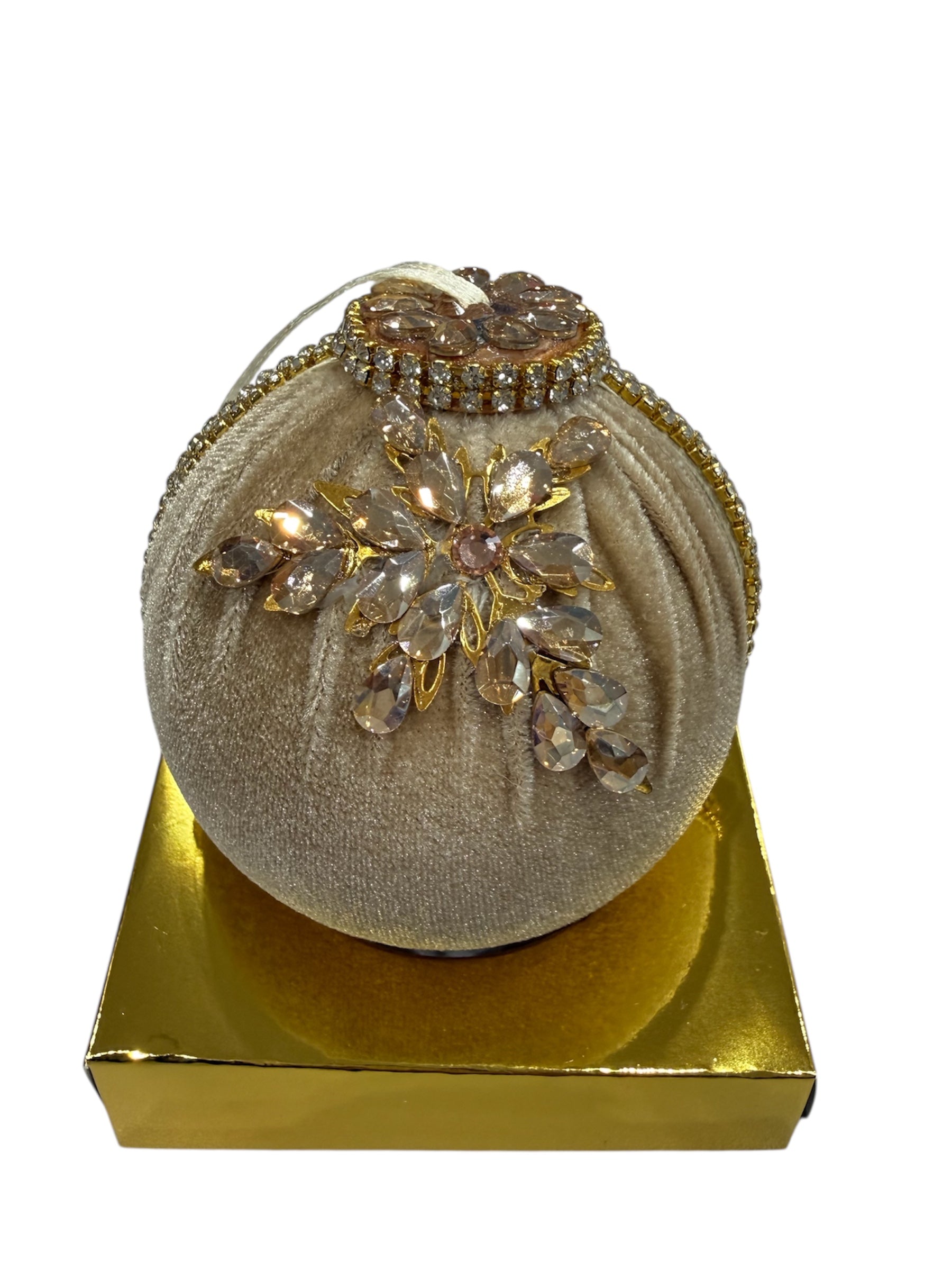 A round, velvet Christmas ornament with rhinestone and gold embellishments sits on a gold box.