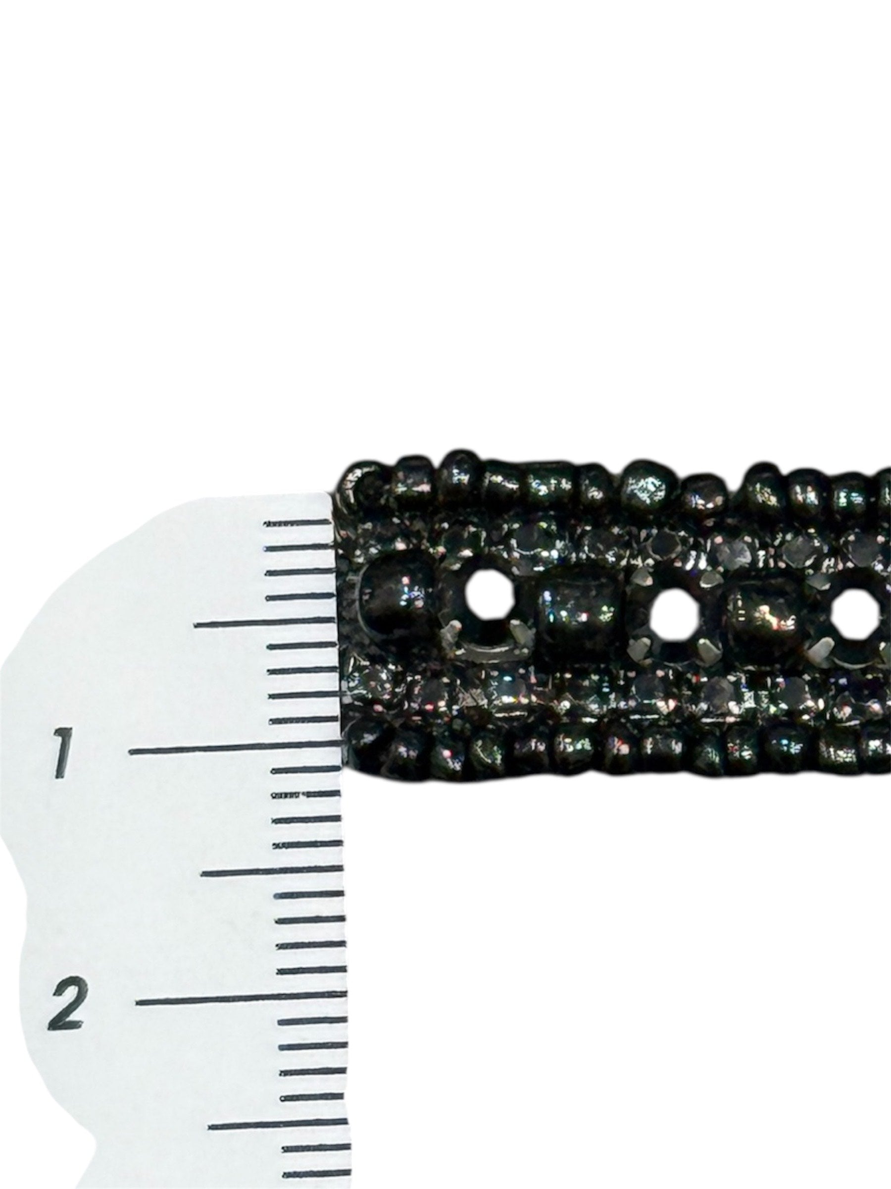 Black embroidered fabric trim with a repeating pattern and cutouts, measured against a ruler.