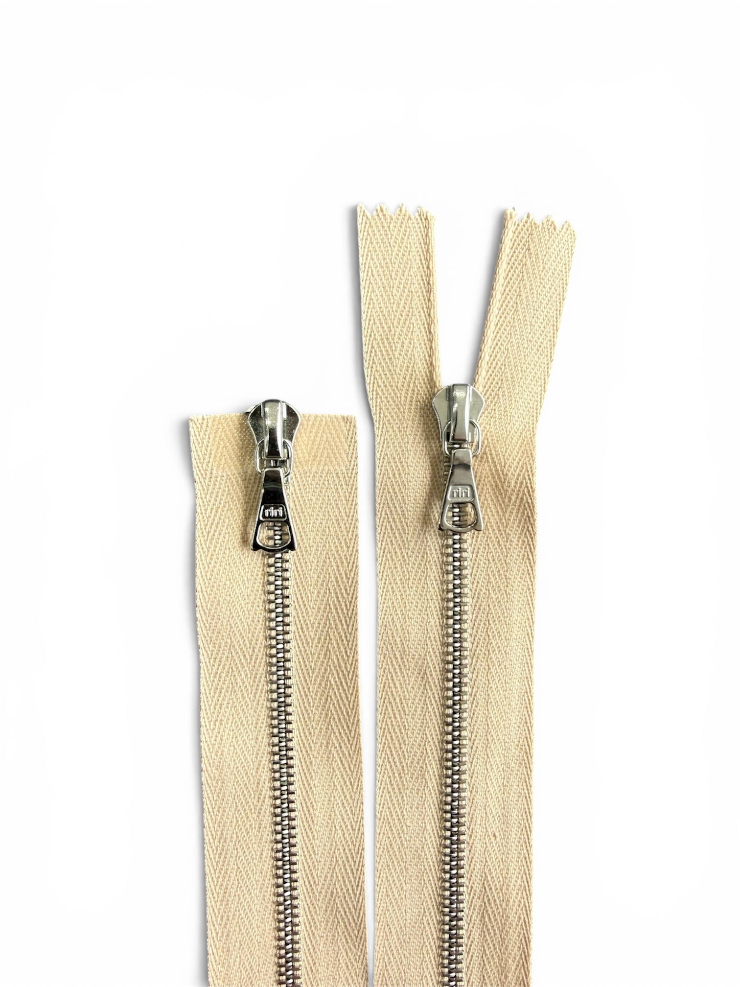 Two Riri cream zippers with silver metal teeth and pulls on a white background.