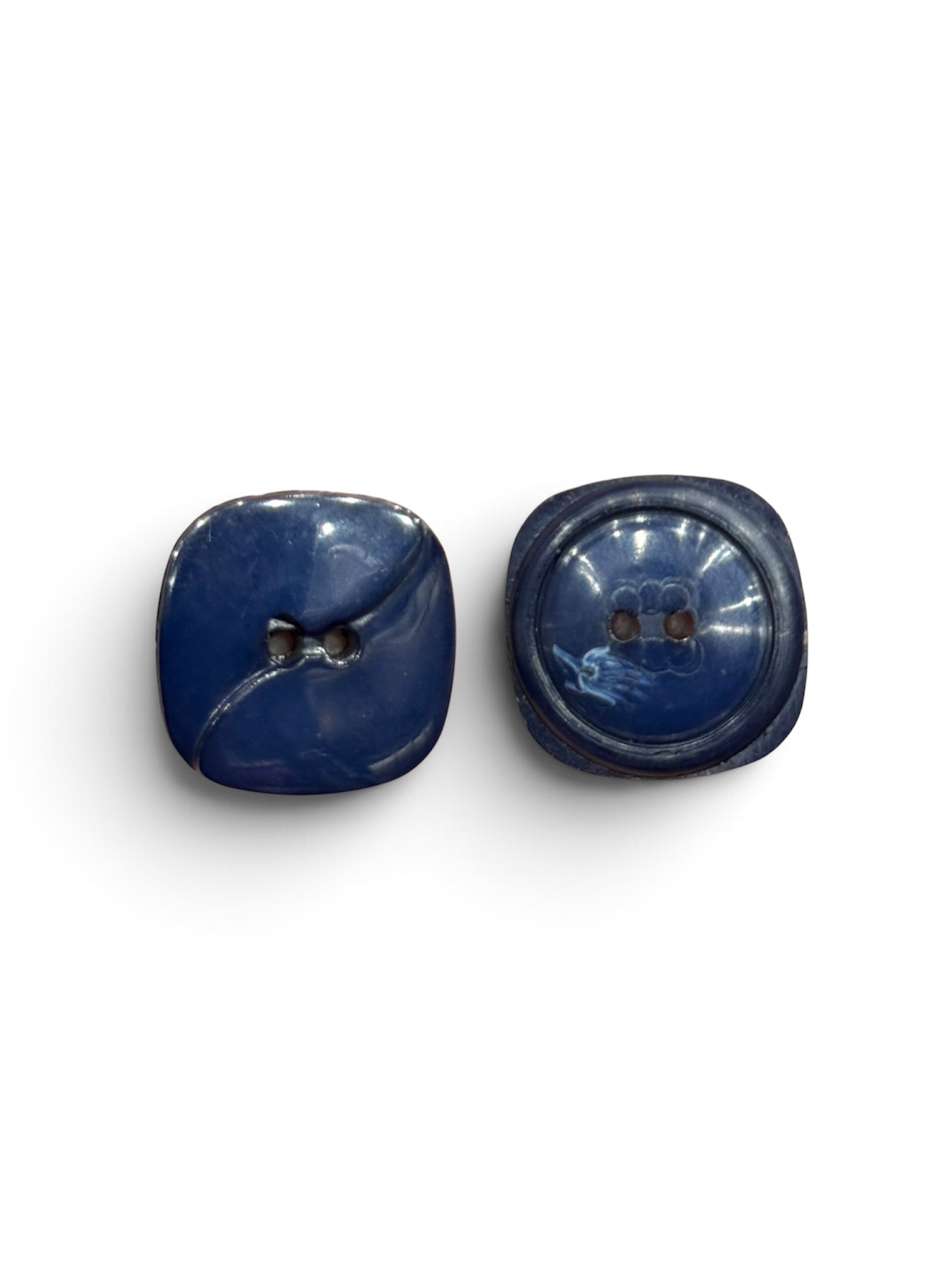 Two navy blue resin 2-hole sewing buttons with a glossy finish and square-round shape.