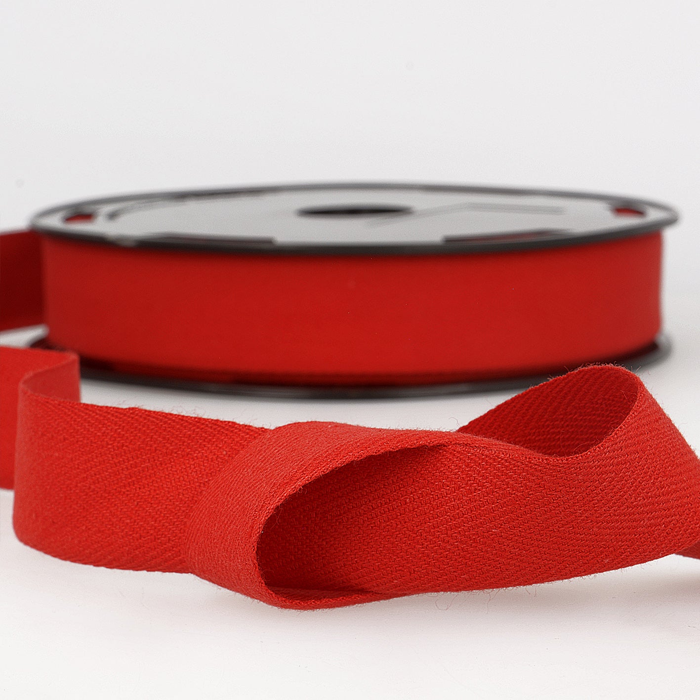 Red cotton twill tape with a herringbone weave shown on a spool and unrolled in the foreground.