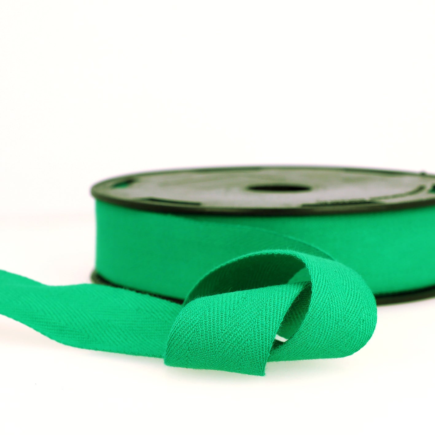 A roll of green cotton twill tape with a herringbone weave on a black spool.