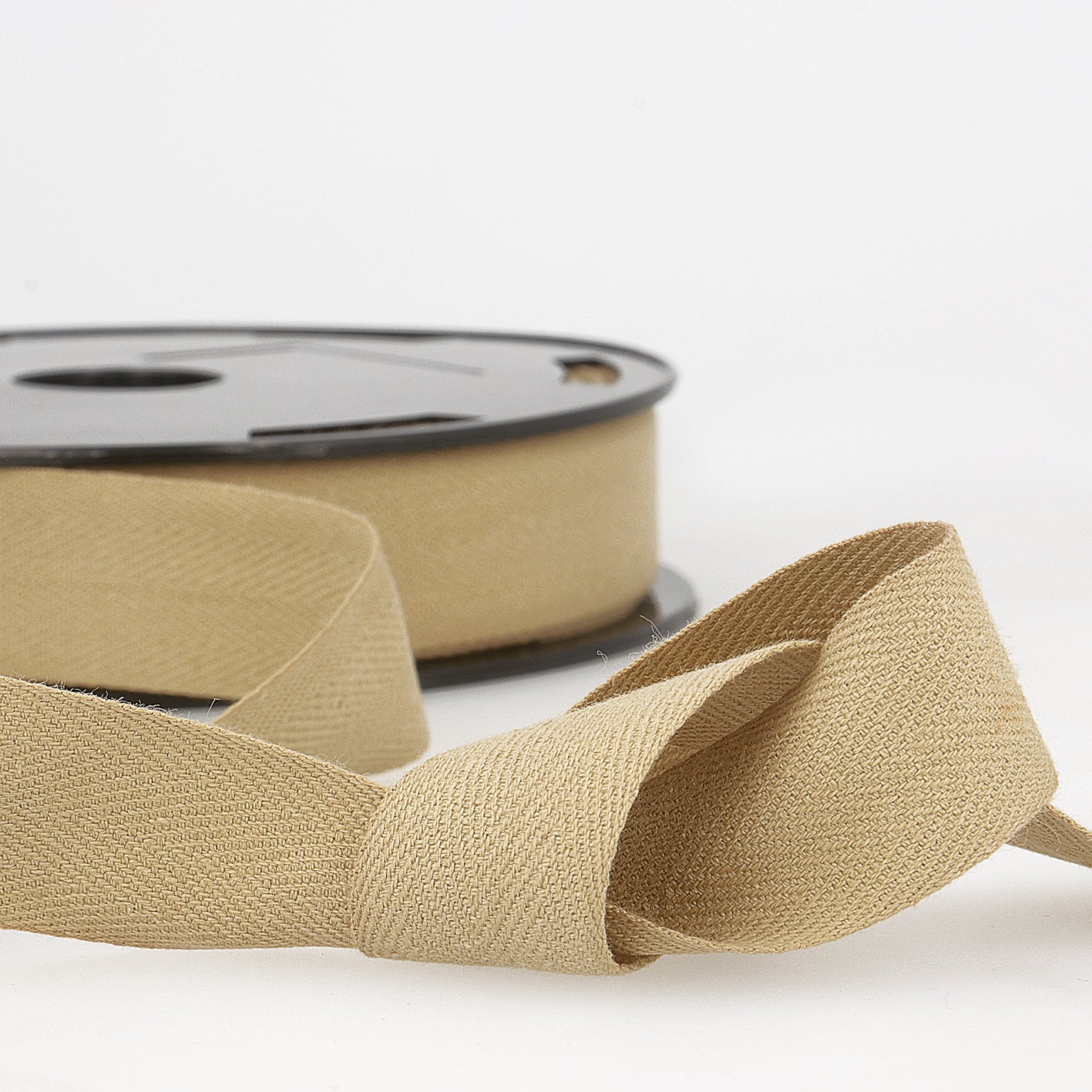 A roll of tan cotton twill tape with a herringbone weave shown in a loose knot.
