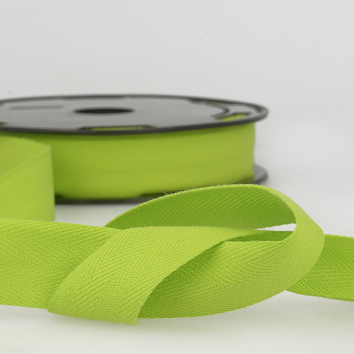 Lime green cotton twill tape with a herringbone weave shown on a spool and loose.