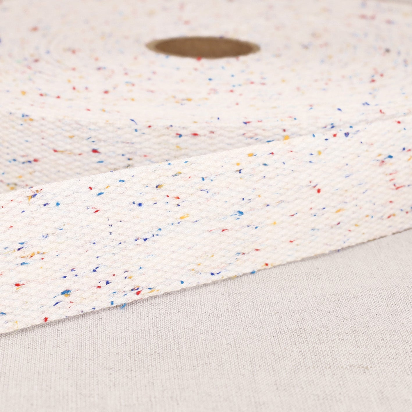 A roll of 20mm white polyester webbing strap with a colorful mottled fleck pattern.