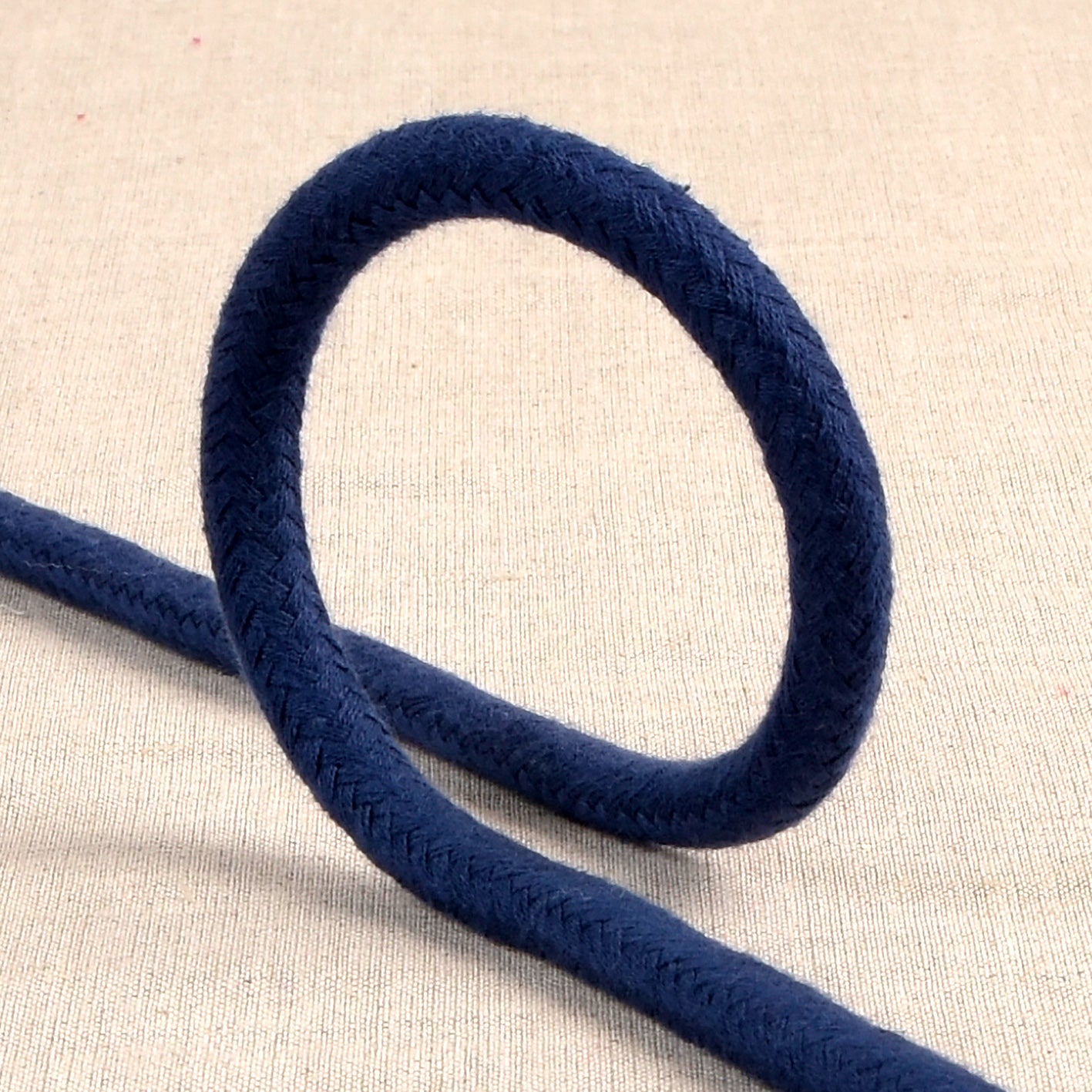 Navy blue 6mm braided cotton cord looped on a neutral fabric background.