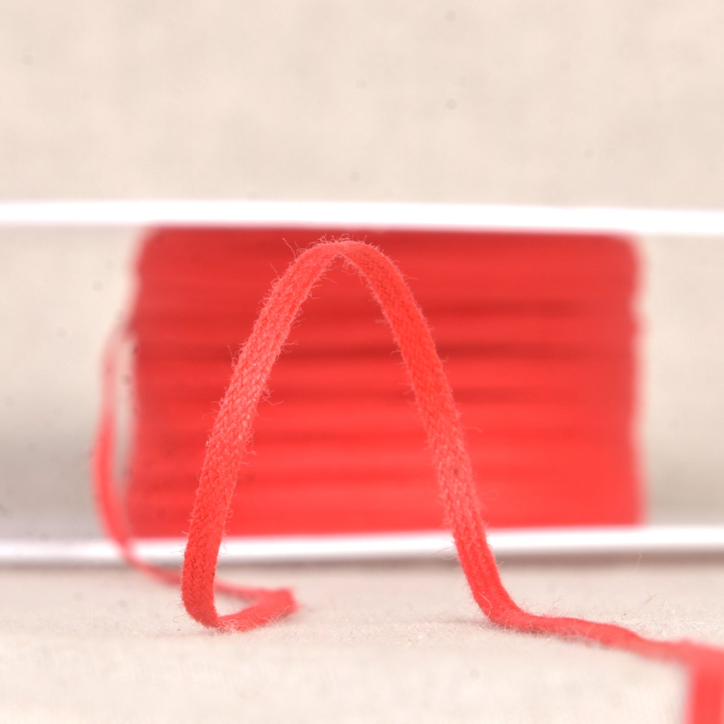 A spool of thin red cotton draping tape for patterning, measuring 3mm wide.