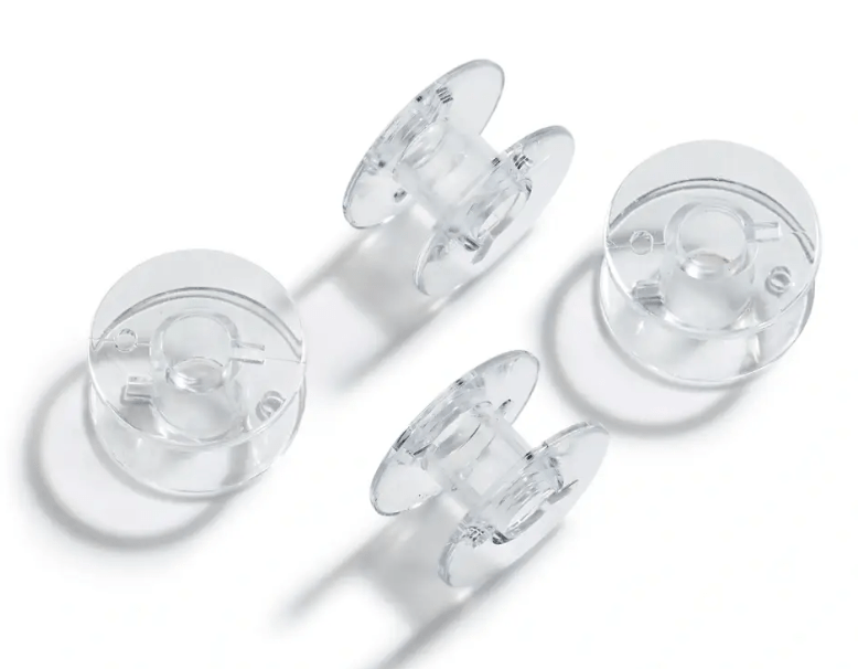 Four transparent plastic sewing machine bobbins on a white background.