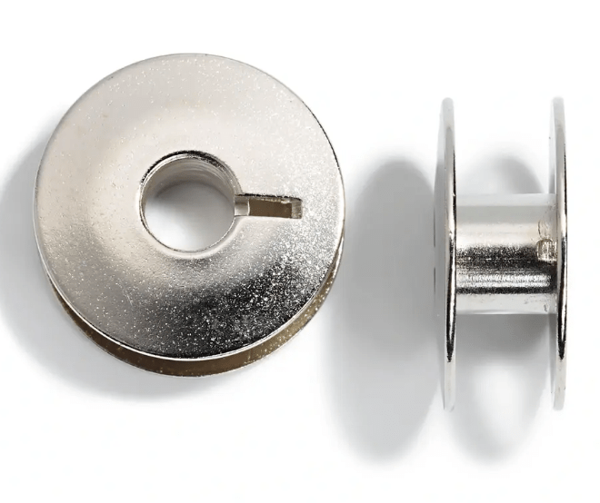 Two silver metal sewing machine bobbins on a white background.