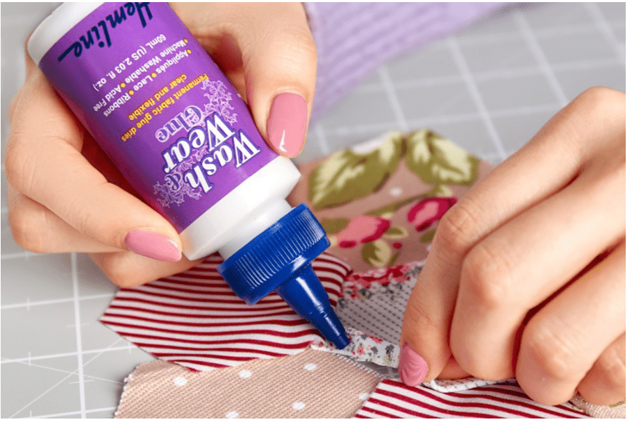 A hand applies Wash & Wear fabric glue from a purple bottle to fabric pieces.