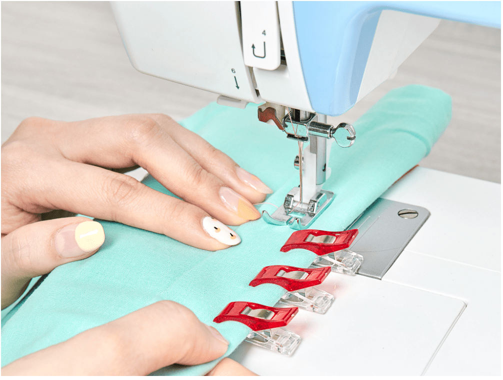 A close-up of a sewing machine with fabric clips holding turquoise fabric.