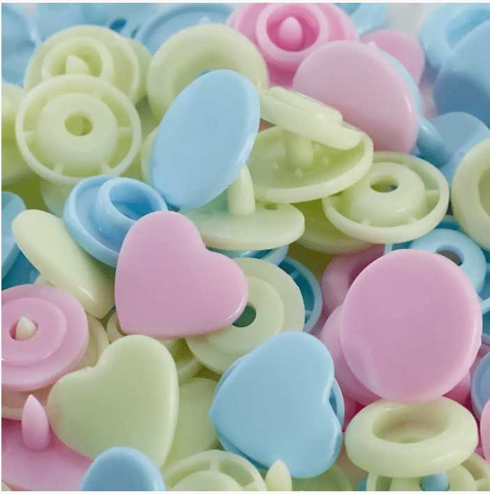 Assorted color plastic snap fasteners in heart and round shapes.