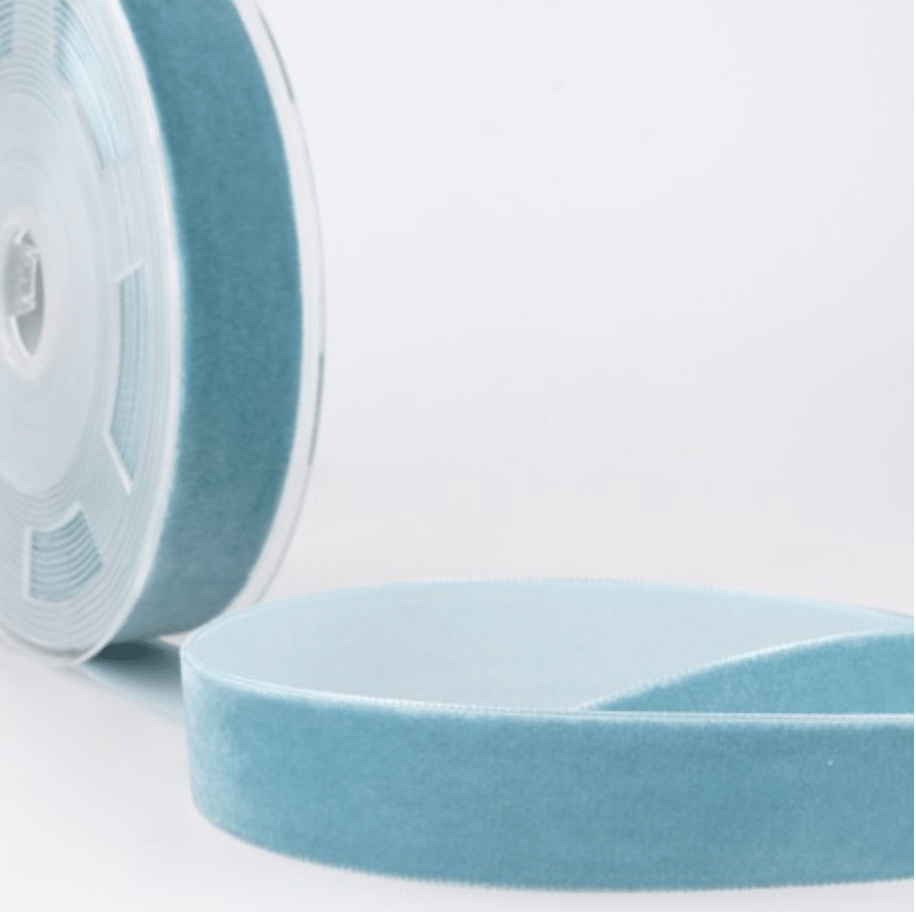 Velvet ribbon in a teal blue color, shown on a spool and unrolled.