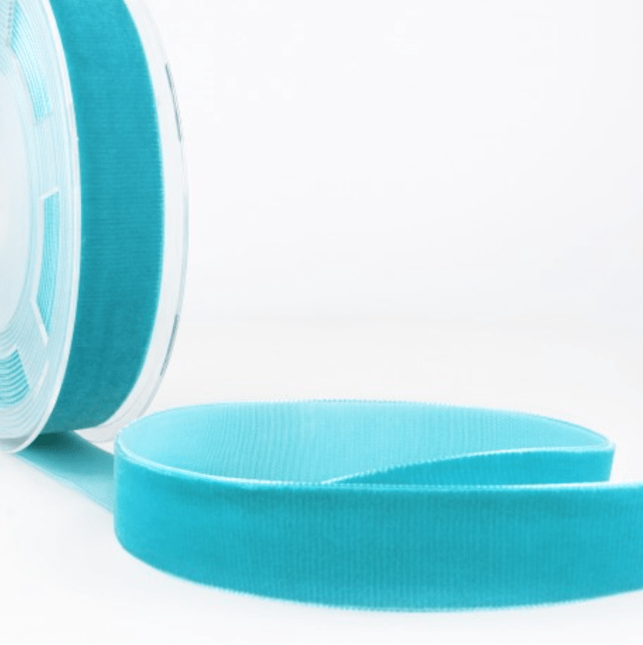 Turquoise velvet ribbon on a spool, with a length of ribbon unspooled.