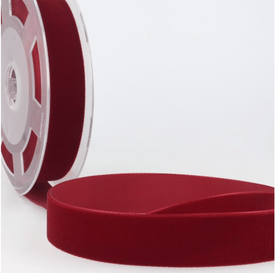 A roll of dark red velvet ribbon with a portion of the ribbon unrolled in the foreground.
