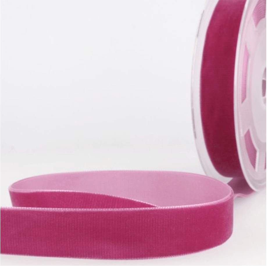 Velvet ribbon in a deep pink color, coiled and on a spool.
