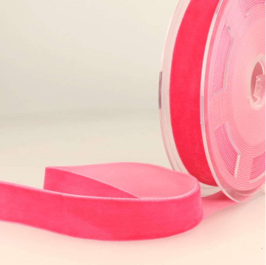 A roll of bright pink velvet ribbon with a section unspooled.