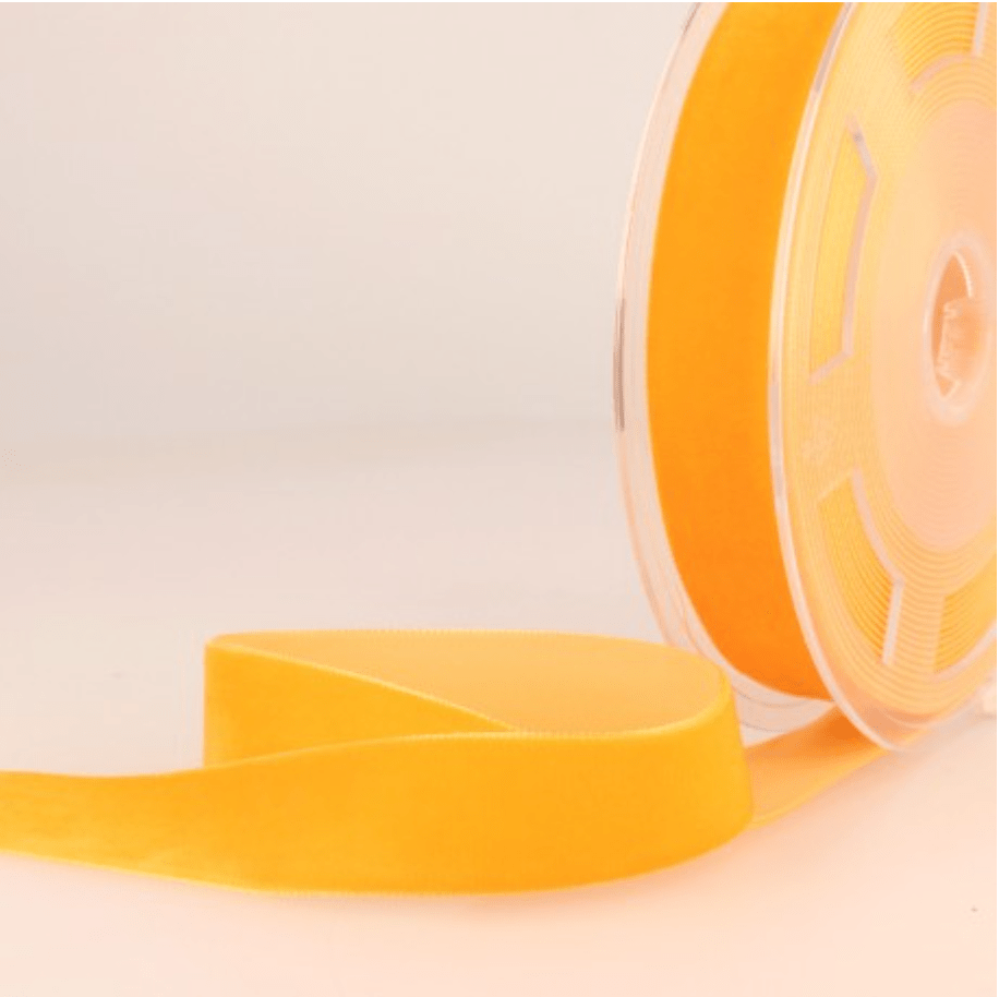 A roll of orange velvet ribbon with a length of ribbon unspooled.
