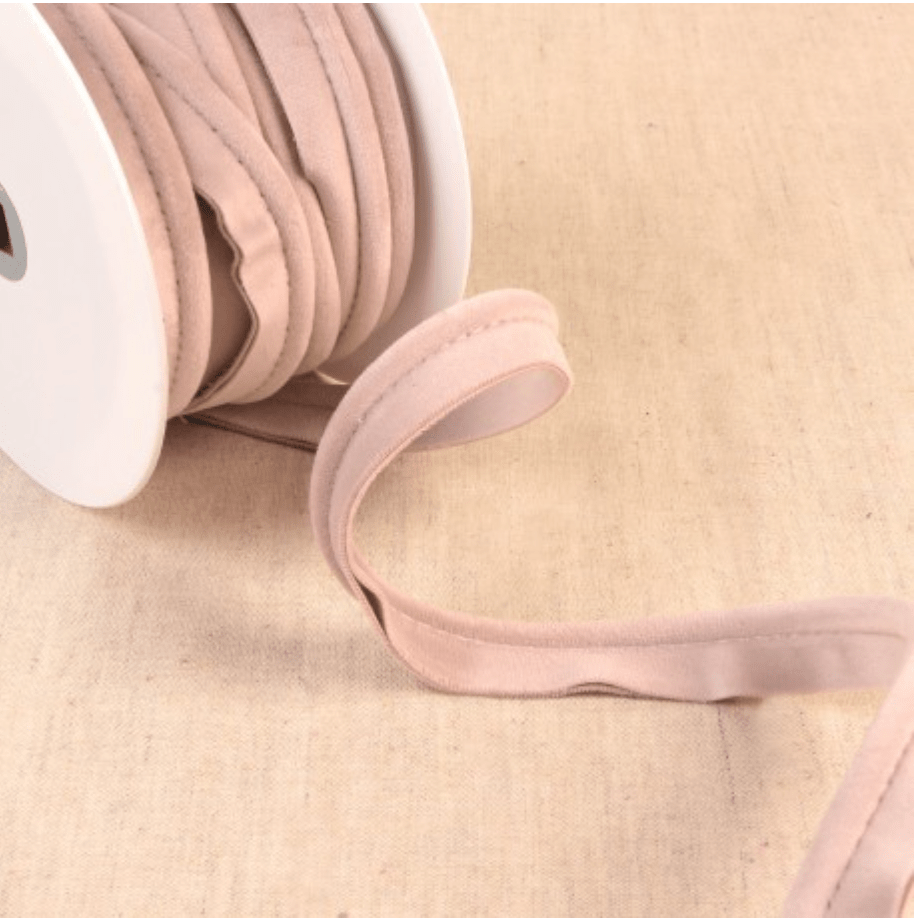 A roll of light pink velvet piping cord with a portion unspooled.