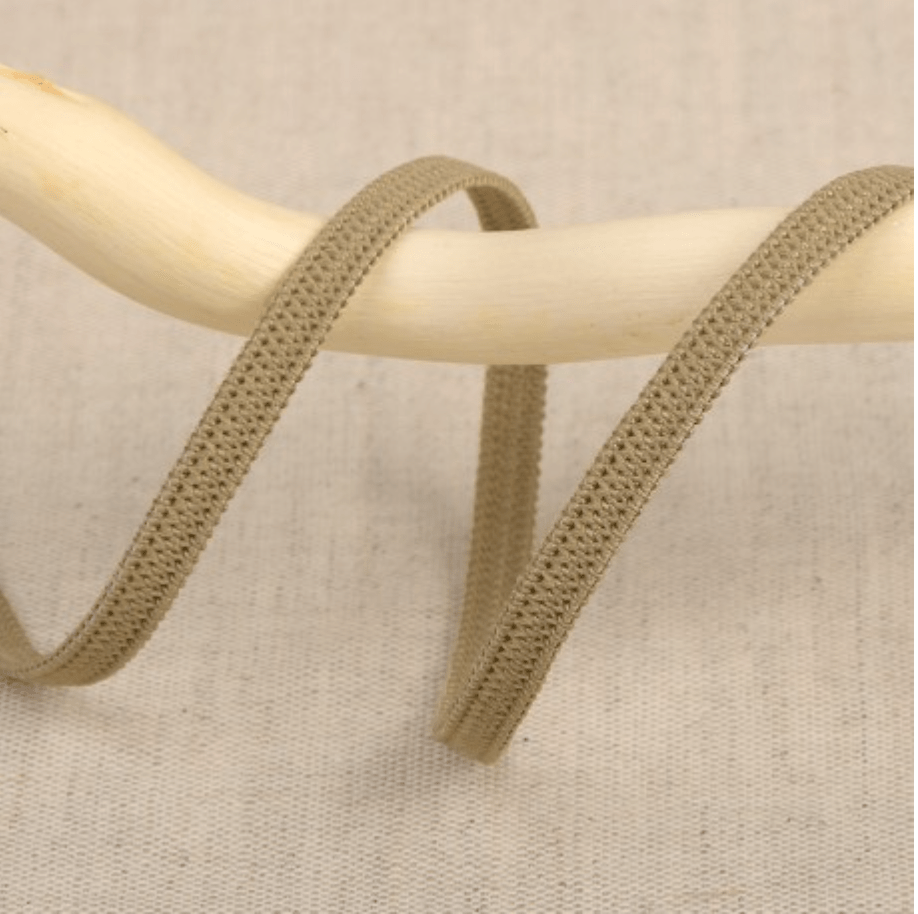A beige elastic ribbon with a textured pattern is draped over a wooden stick.