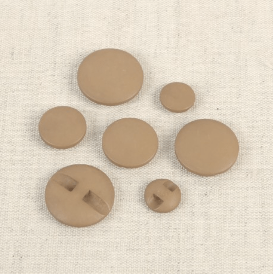 Set of seven round, tan polyester buttons in various sizes.