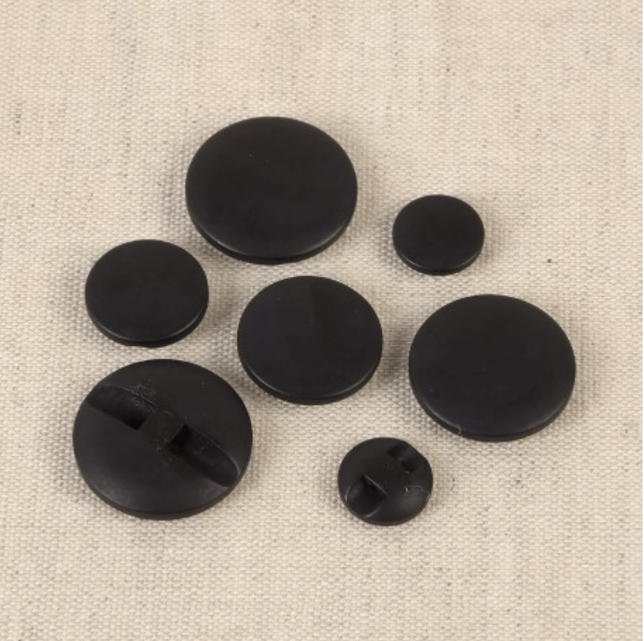 Set of seven black polyester buttons of varying sizes on a textured background.