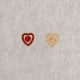 Two heart-shaped buttons, one red and one gold, on a light fabric background.