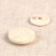 Two round, cream-colored buttons made from rice husk and polyester blend on a neutral fabric.