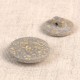 Two round, textured grey buttons made from a rice husk and polyester blend on a neutral background.