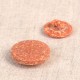 Two round, textured orange buttons made from a blend of rice husk and polyester.