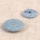 Two light blue, speckled eco-friendly rice husk and polyester buttons on a neutral fabric surface.