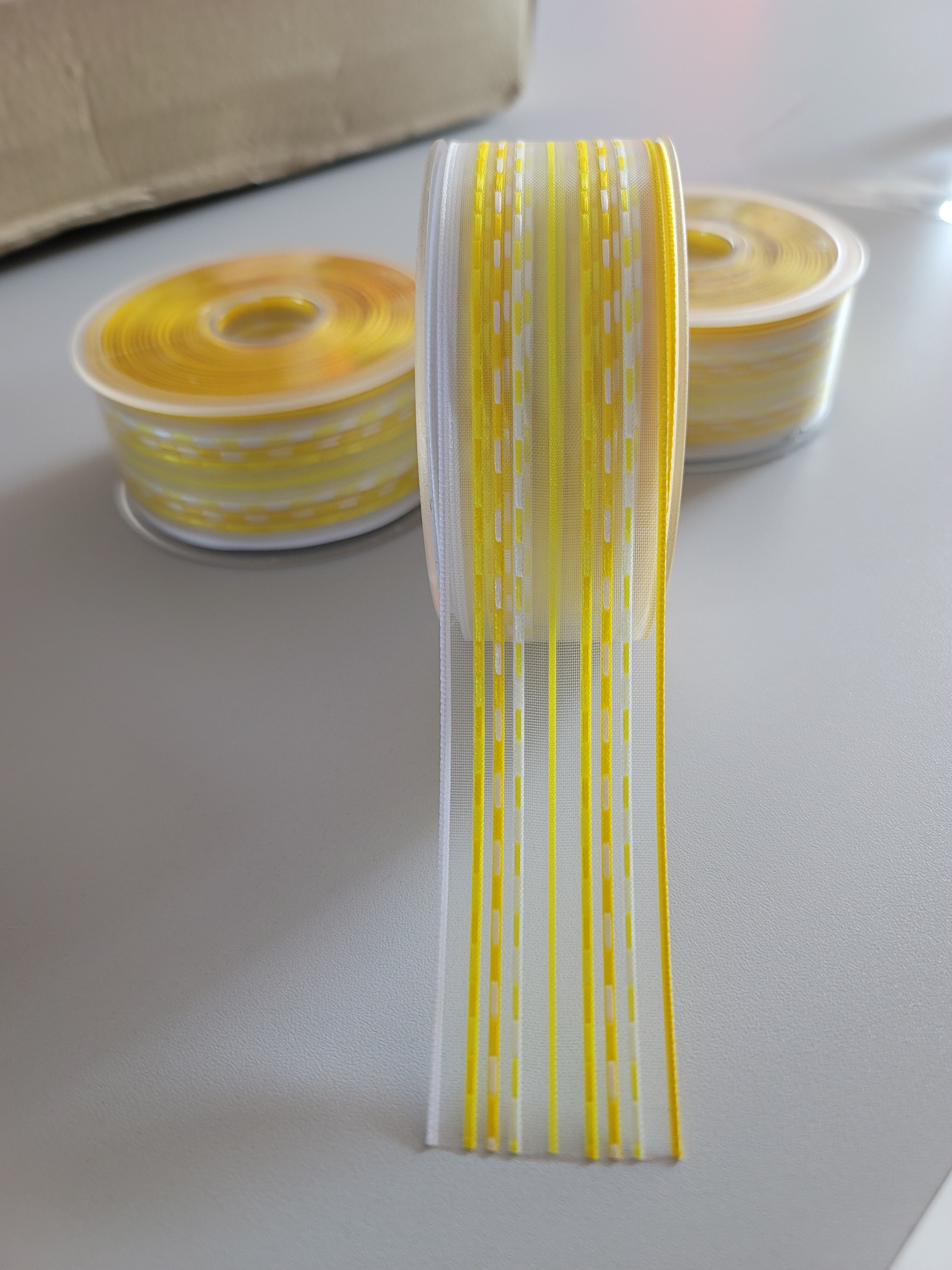 Roll of 40mm yellow and white striped chiffon Elba ribbon tape on a gray surface.