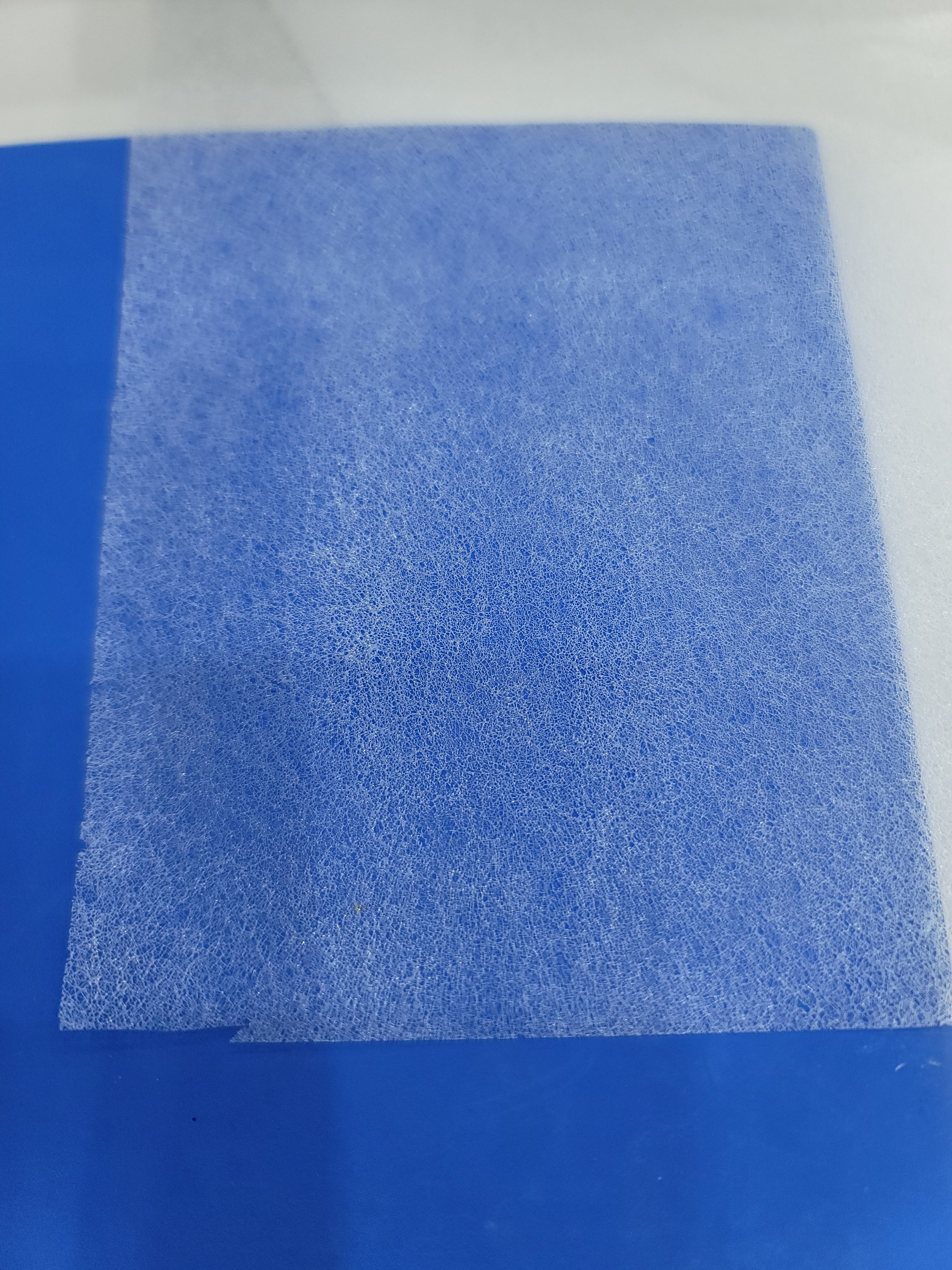 A close-up of the textured, white Wonder Web iron-on bonding web against a blue background.