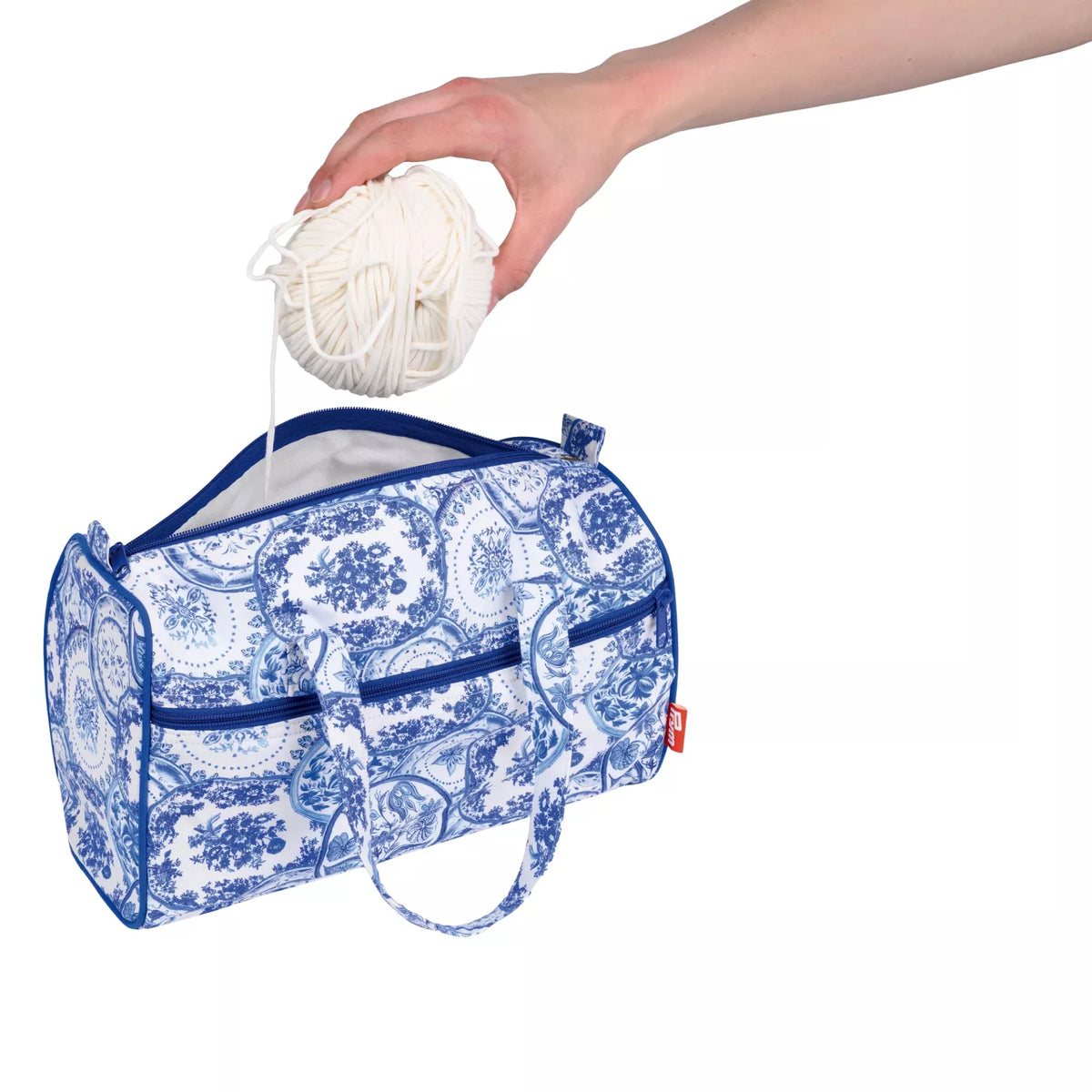 Delft Blue project bag with a hand placing a ball of white wool into the open main compartment.